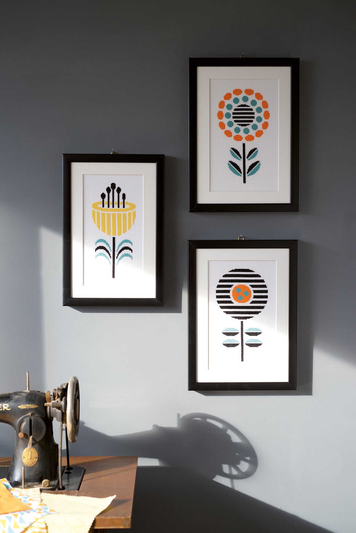Framed cross stitch of a striped black flower with orange centre and teal leaves