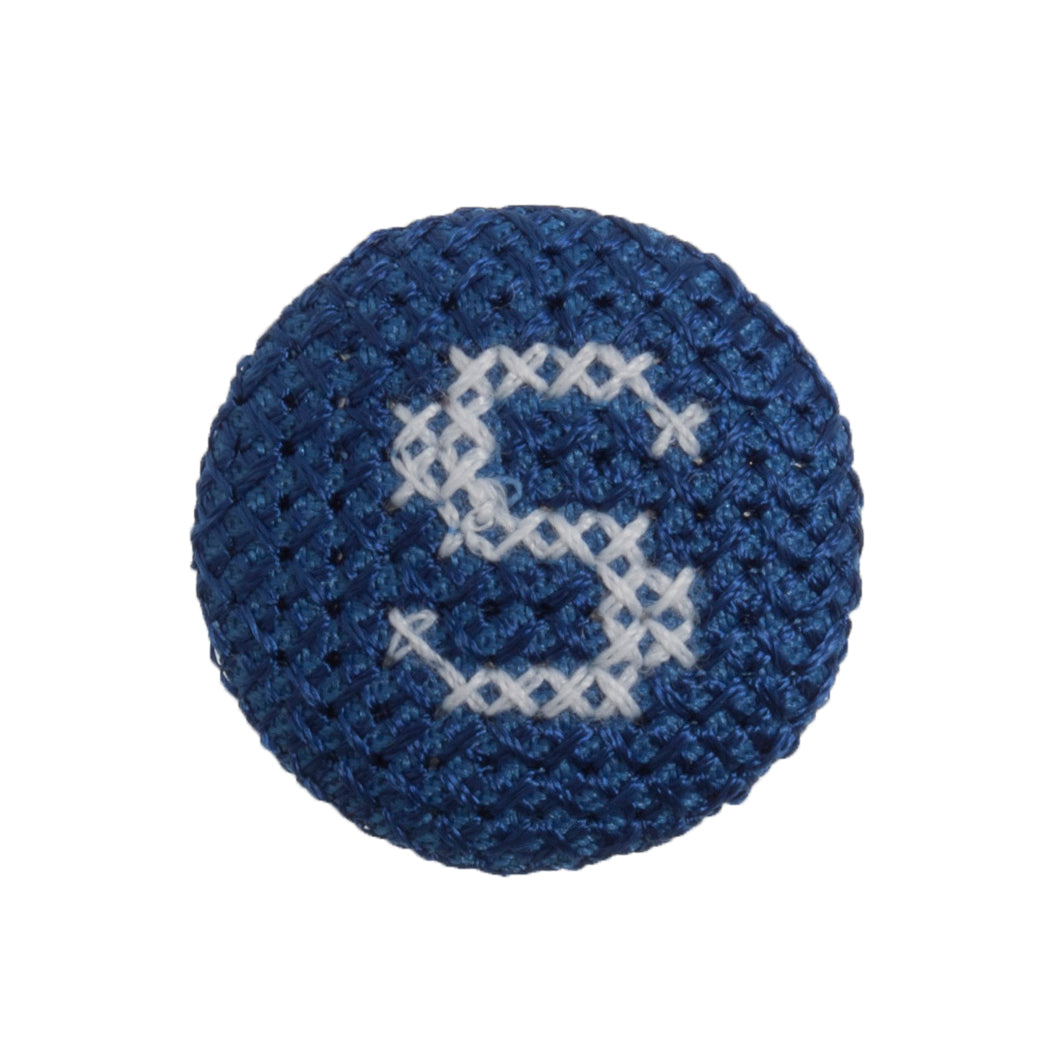 Round navy blue fabric button with a white cross stitch letter S