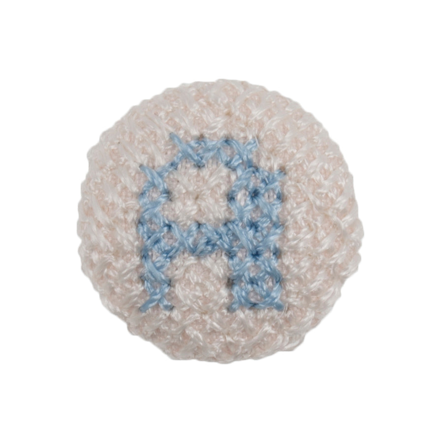 Round white fabric button with a light blue cross stitch letter A