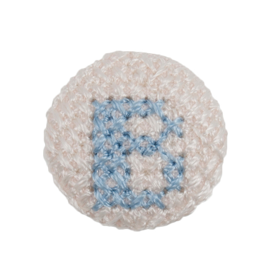 Round white fabric button with a light blue cross stitch letter B