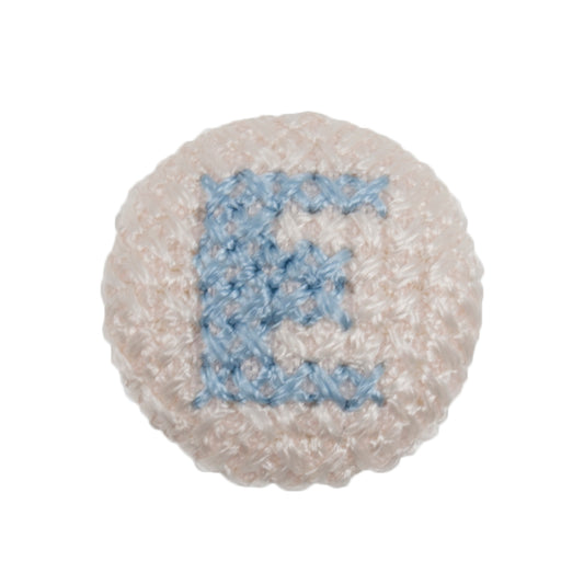 Round white fabric button with a light blue cross stitch letter E