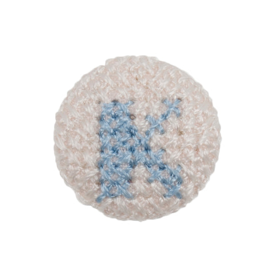 Round white fabric button with a light blue cross stitch letter K