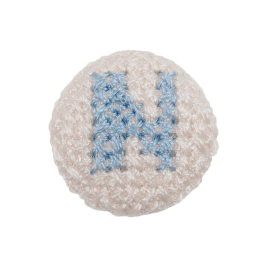 White fabric-covered button with a light blue cross-stitched letter N