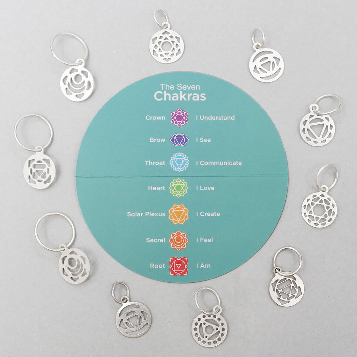 Silver plated ring stitch markers with chakra symbol charms beside a fabric pouch