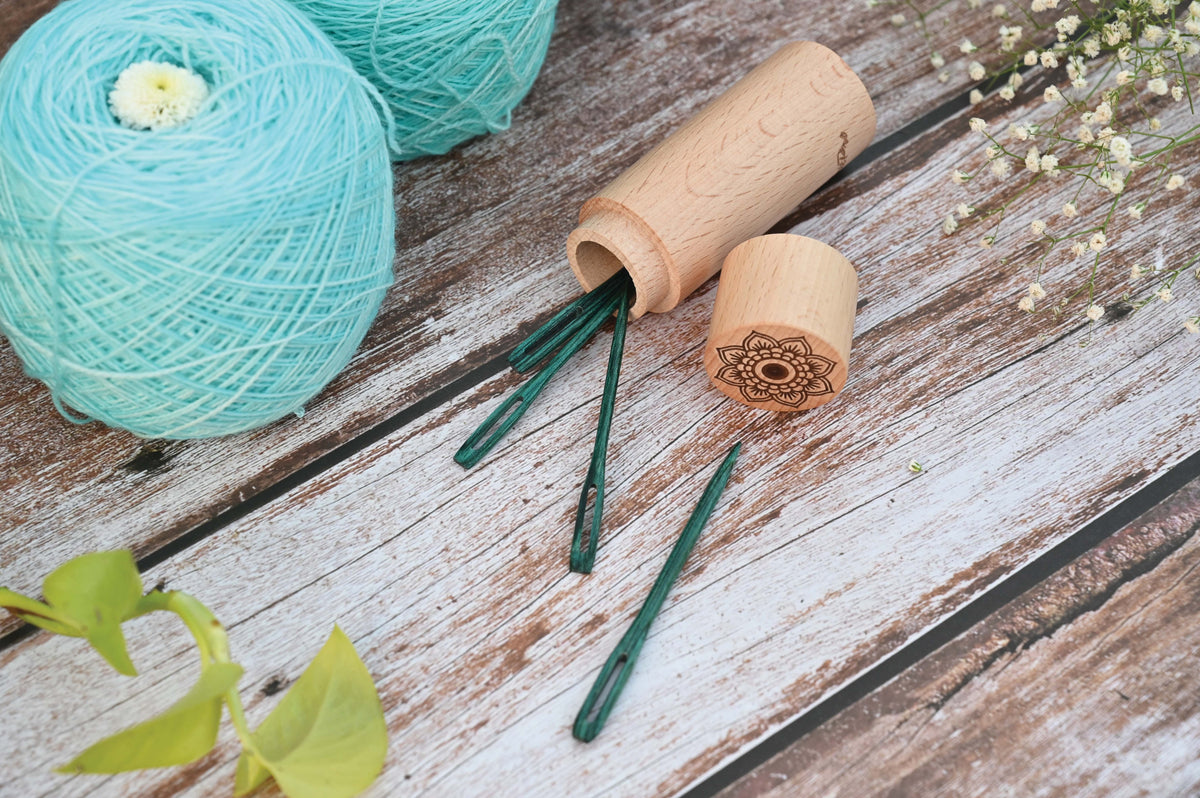 Four teal wooden darning needles beside a round wooden case