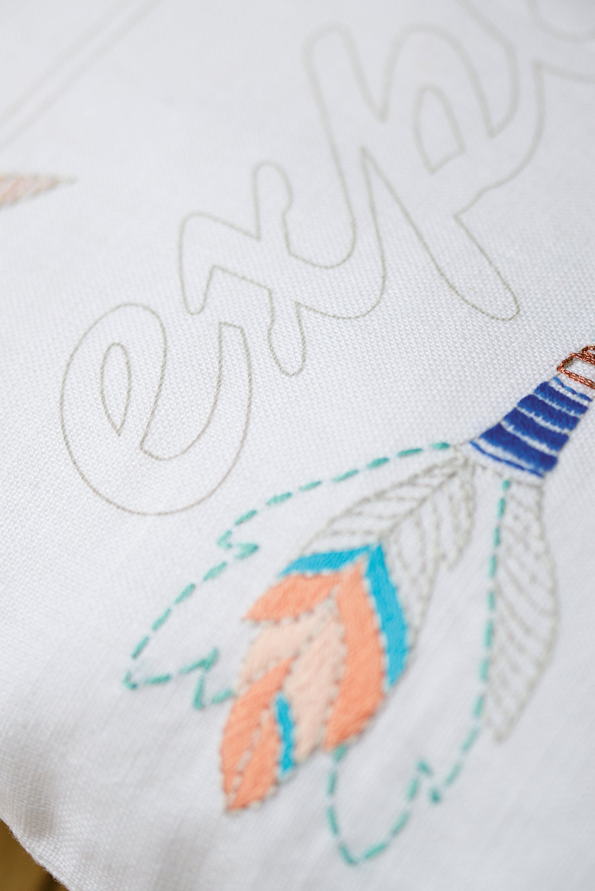 Embroidered cushion with arrow design and the word Explore