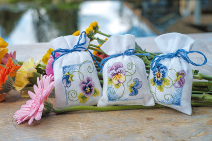 Three violet cross stitch gift bags tied with ribbon
