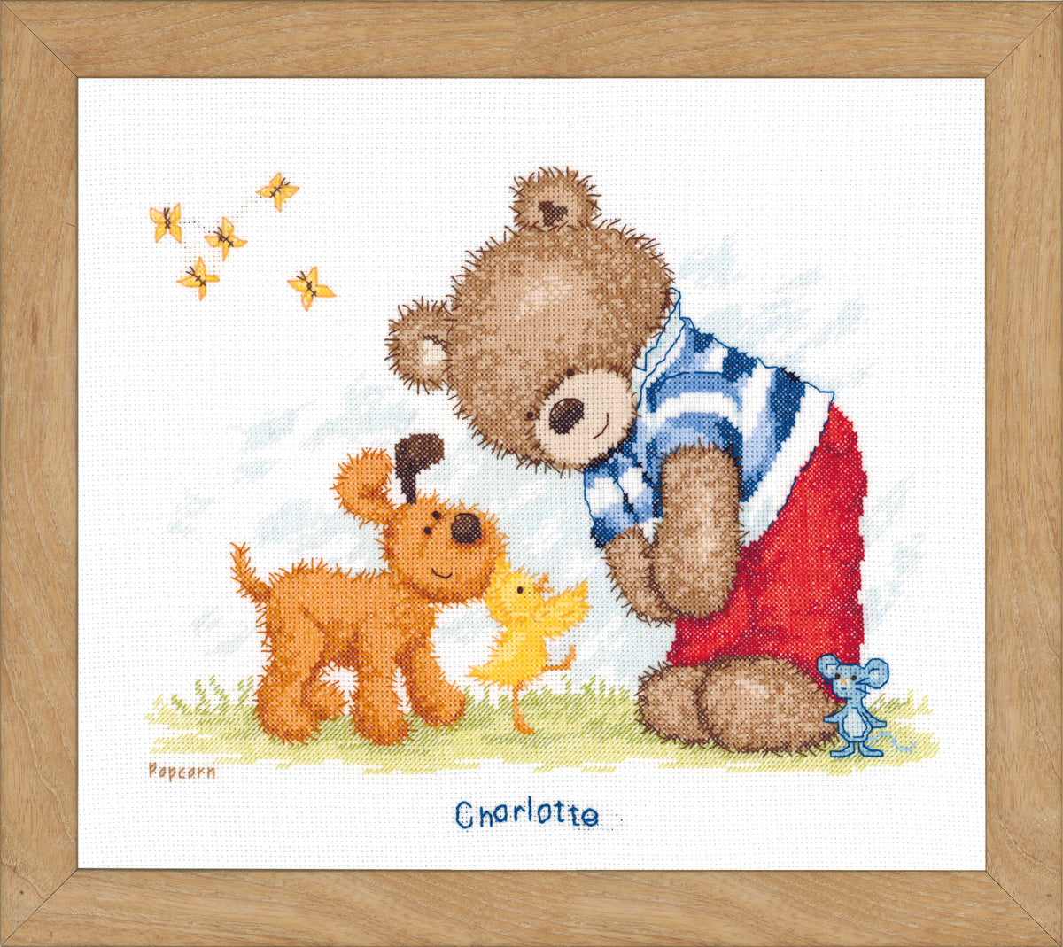 Cross stitch of Popcorn the bear in a garden