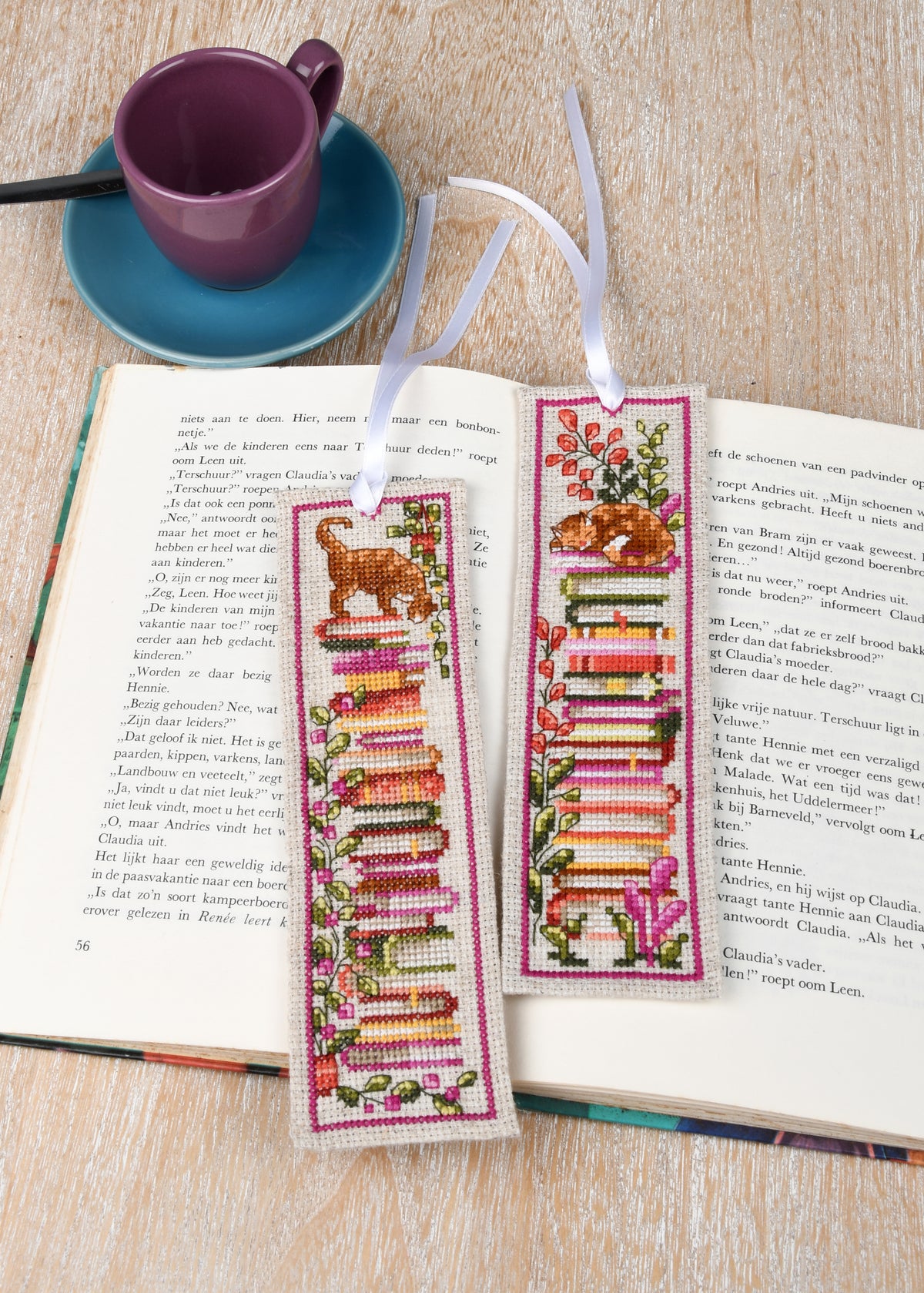 Two cross stitched bookmarks with cats sitting on stacks of books