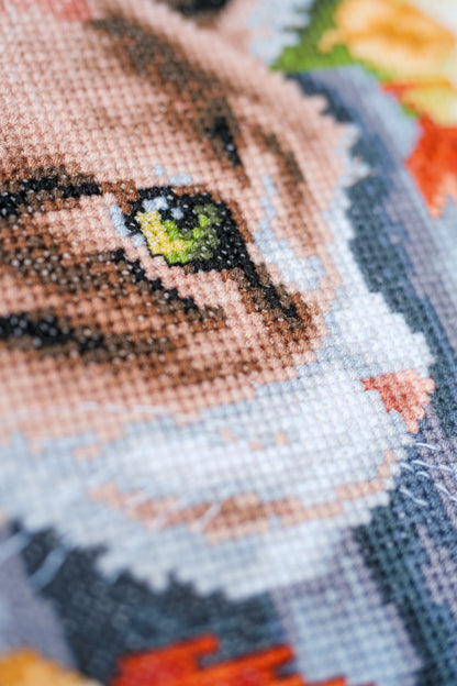 Cross stitch picture of a kitten by a garden fence