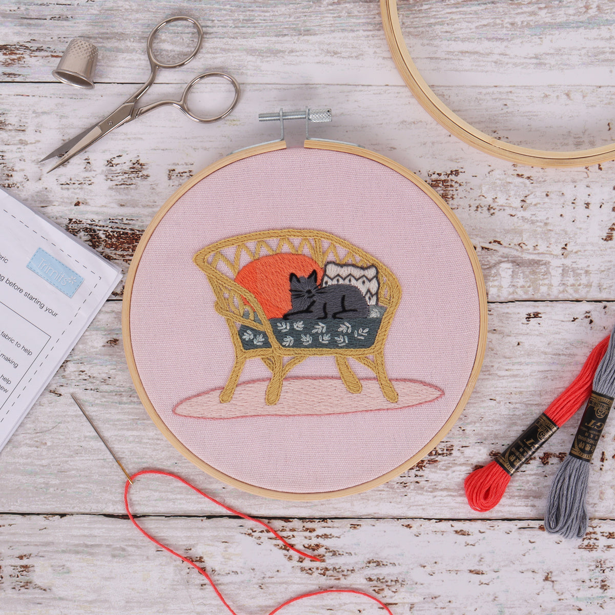 Embroidery hoop kit showing a stitched cat on wicker chair design