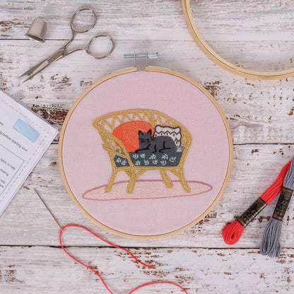 Embroidery hoop kit showing a stitched cat on wicker chair design