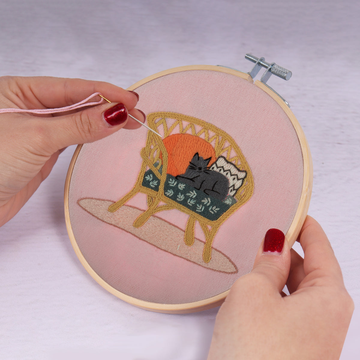 Embroidery hoop kit showing a stitched cat on wicker chair design